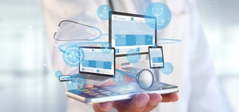  Hand holding a smartphone projecting holographic medical website interfaces across laptop, tablet, and desktop screens with healthcare icons and digital connectivity elements. 