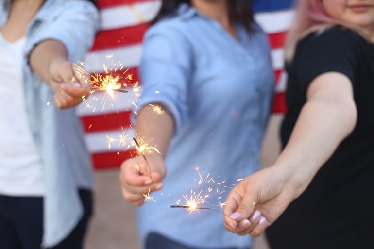 image of women holding sparklers with american flag behind
