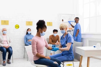  healthcare nurse practioner distributing COVID-19 vaccine to woman in health clinic 